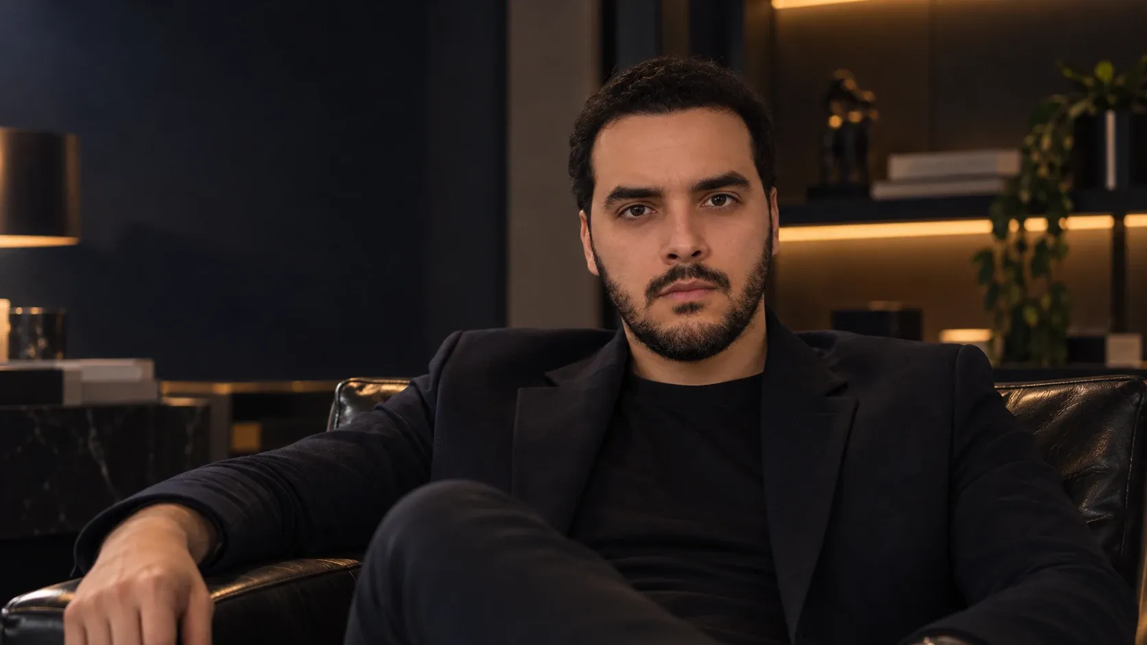 Cauê Oliveira sentado numa poltrona de couro, de blazer preto